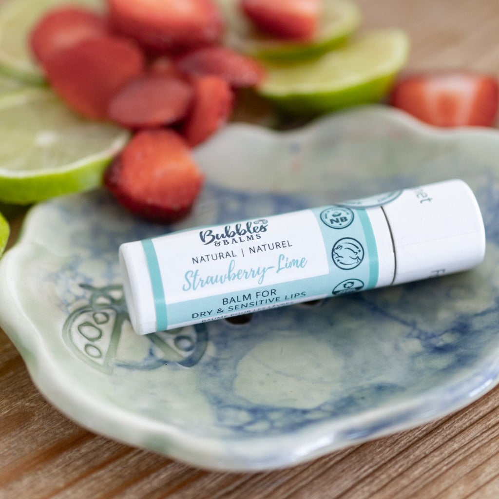 Bubbles & Balms Strawberry Lime vegan lip balms sitting on a custom soap dish with strawberries and limes nearby.