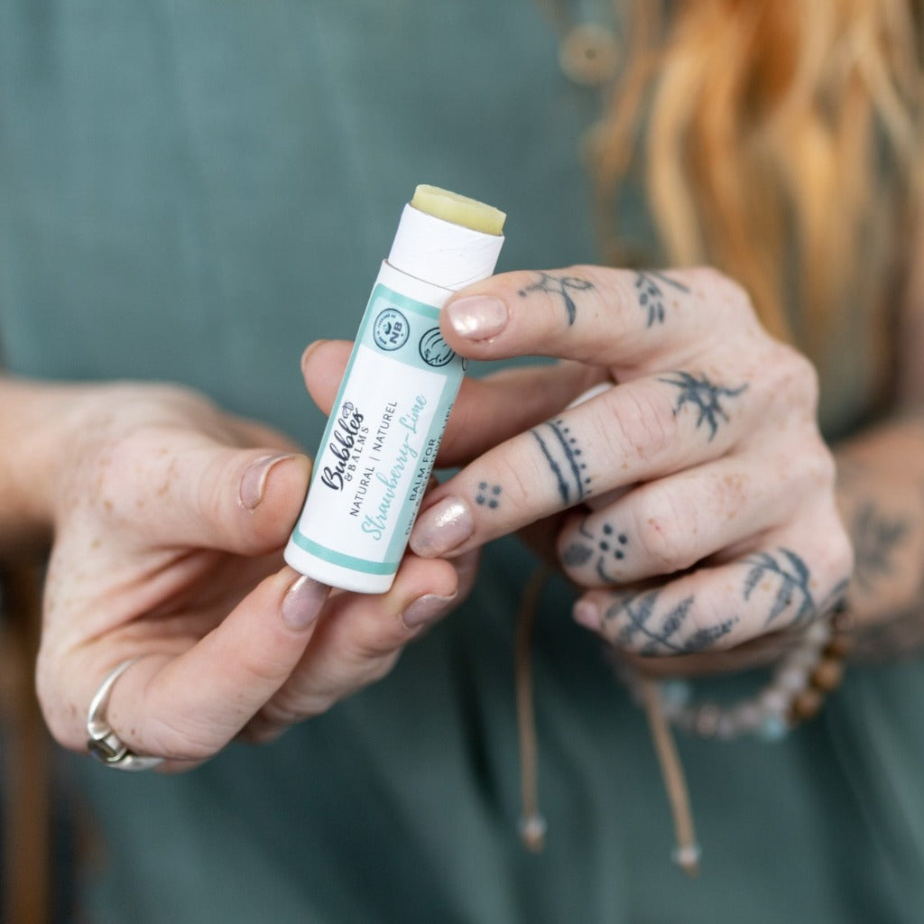 Strawberry Lime vegan lip balm from Bubbles & Balms having the bottom of tube pushed up by woman with tattos and sensitive skin so the lip balm can be used.