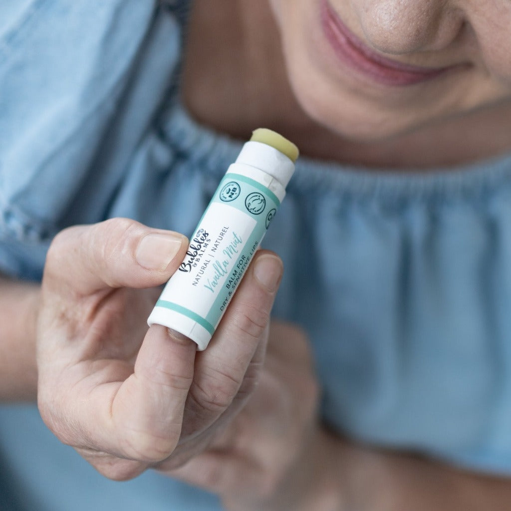 Vanilla Mint vegan lip balm with bottom of tube pushed up slightly so the balm is out of the tube enough to be applied to the smiling, sensitive lips next to it.