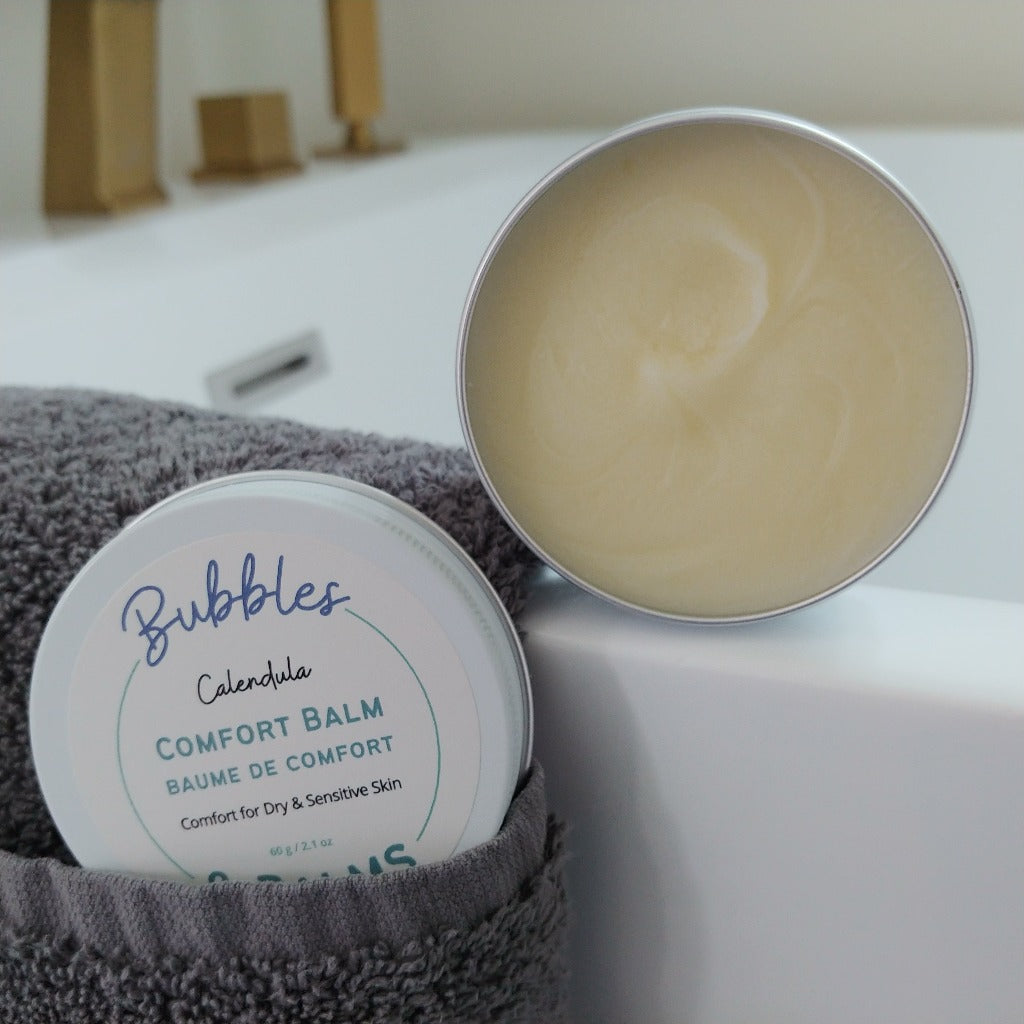 Calendula Comfort Balm from Bubbles & Balms open and ready for use on dry, cracked skin beside a beautiful tub.