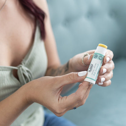 Woman pushing vegan lip balm up from bottom of compostable, zero-waste tube.