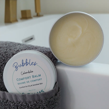 Calendula Comfort Balm from Bubbles &amp; Balms open and ready for use on dry, cracked skin beside a beautiful tub.