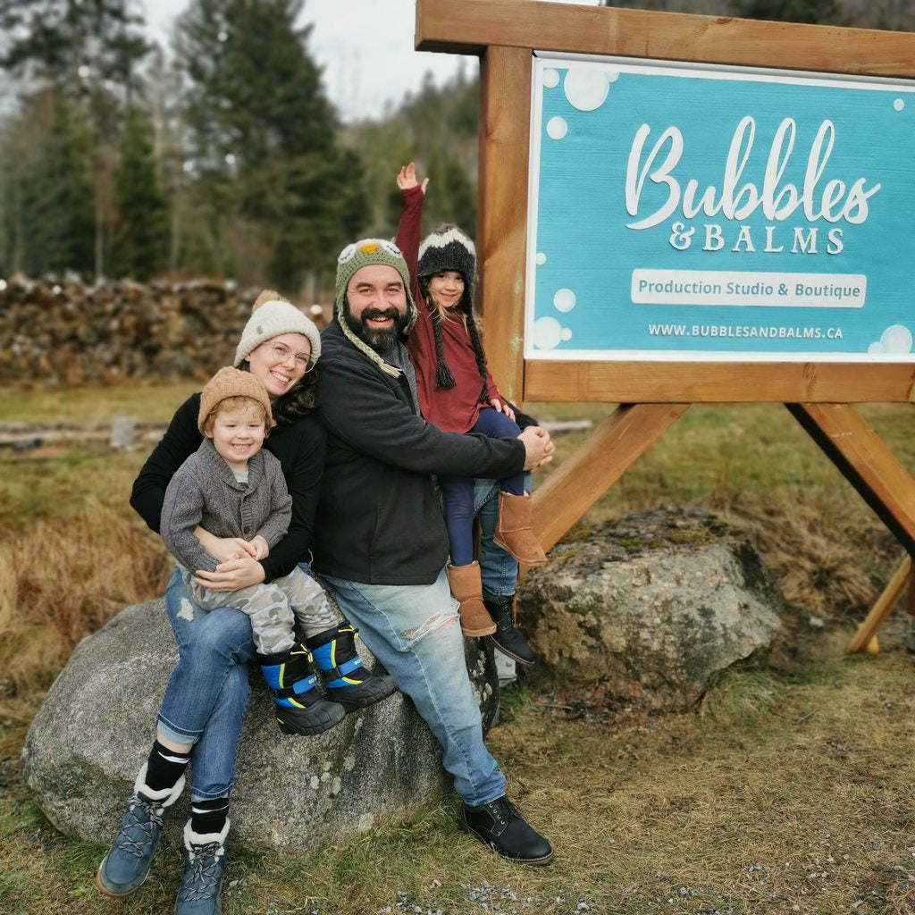 Bubbles & Balms Cofounders Judith & Justin Sweeney Sitting By Roadside Sign for Bubbles & Balms Production Studio & Boutique